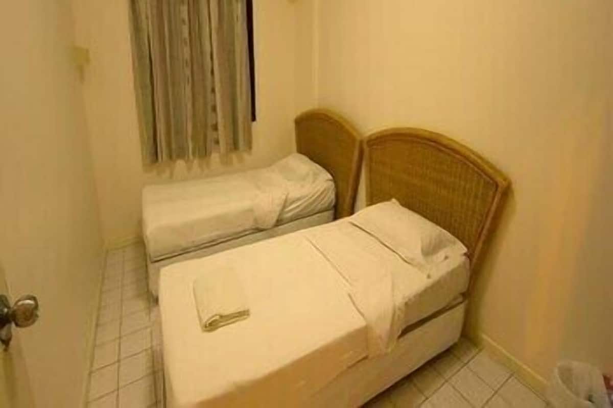 A small, single-room hotel room with a bed, a bedside table, and a window with curtains.