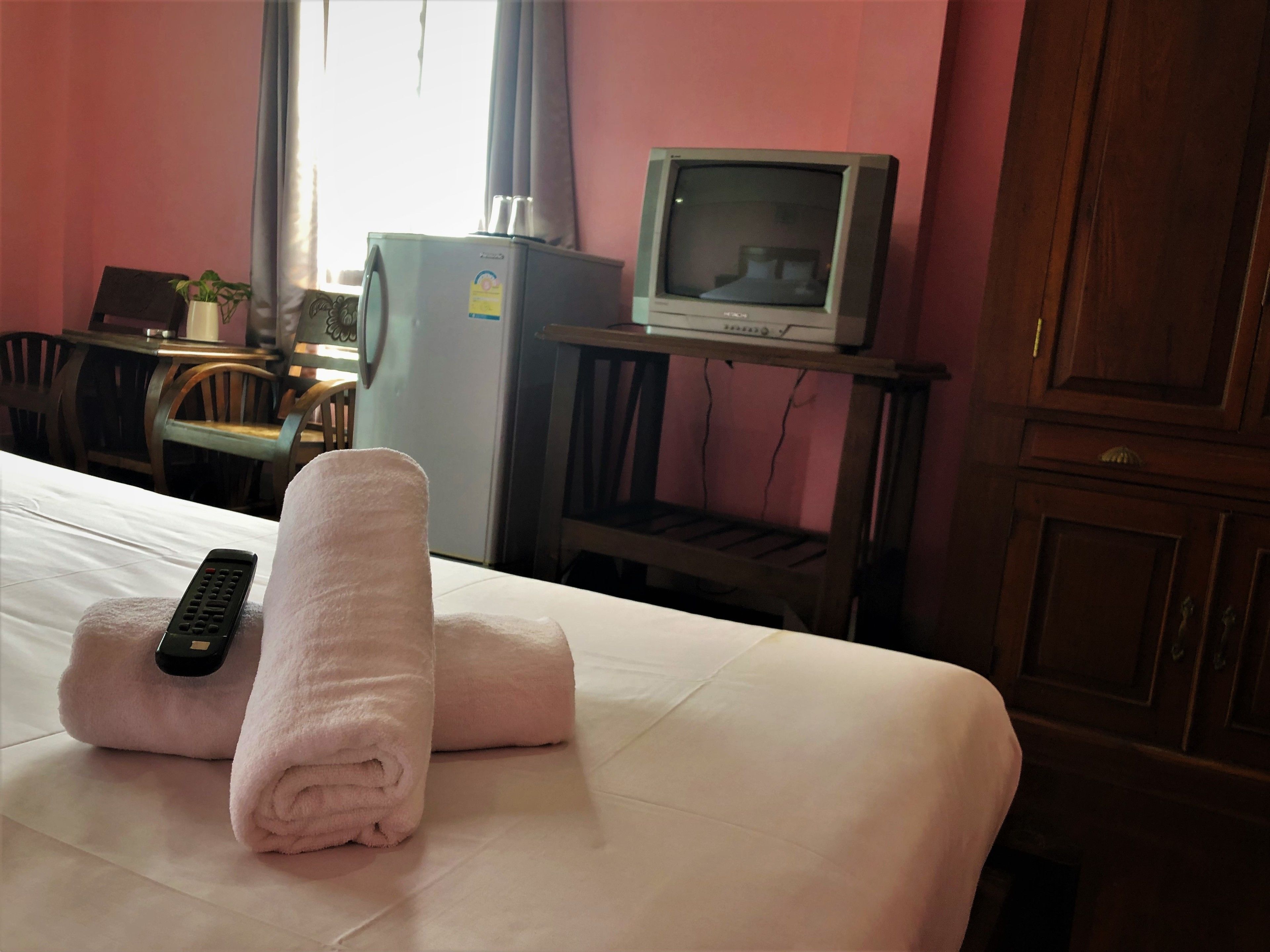 A hotel room with a bed, a remote control, and a television on a wooden stand.