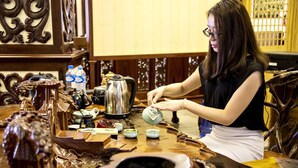 A person pouring tea into a cup at a wooden table with various tea sets and a kettle. - Dansavanh Vientiane Hotel (Vientiane)