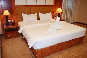 A double bed with white linens, two bedside tables with lamps, and a wooden headboard. - Dansavanh Vientiane Hotel (Vientiane)