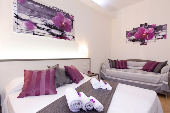 Une chambre d’hôtel avec un lit, un canapé et deux tableaux représentant des orchidées, accrochés au mur.