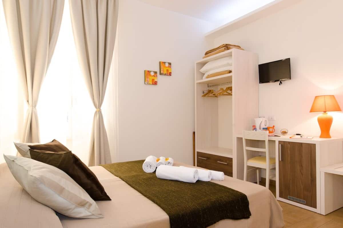 A hotel room with a bed, a desk, a wardrobe, and a TV.