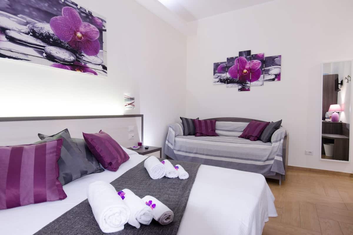 A hotel room with a bed, a sofa, and a small table. There are towels and pillows on the bed.