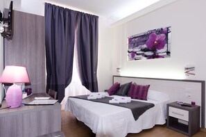 A hotel room with a bed, bedside tables, a desk with a lamp, and a wall-mounted artwork. - Gemme di Roma (Rome)