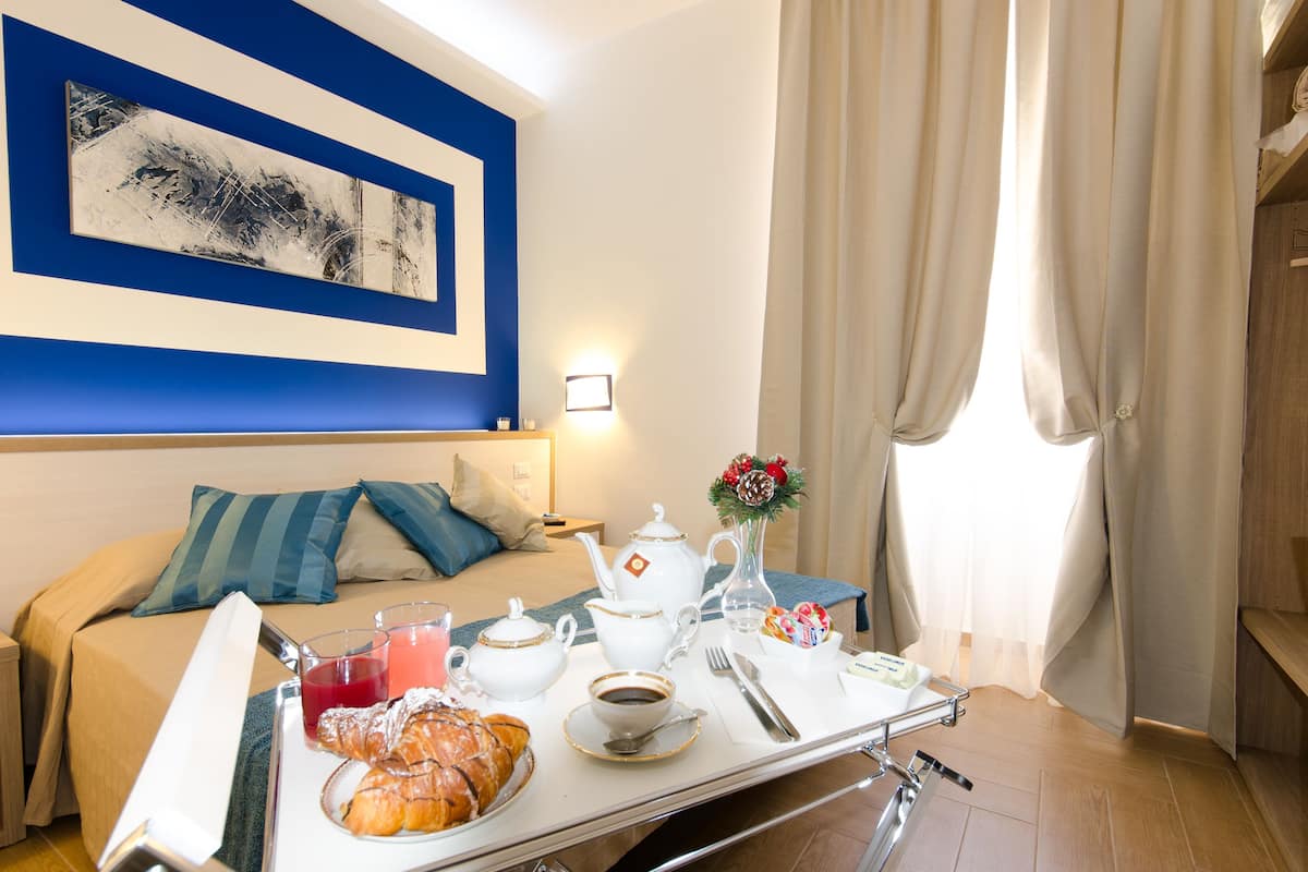 A hotel room with a bed, breakfast tray, artwork, and curtains.