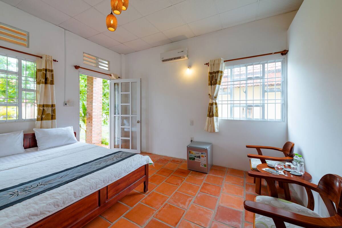 Ein Zimmer mit einem Bett, einem kleinen Tisch mit Stühlen, einem Kühlschrank und einem Fenster mit Vorhängen.
