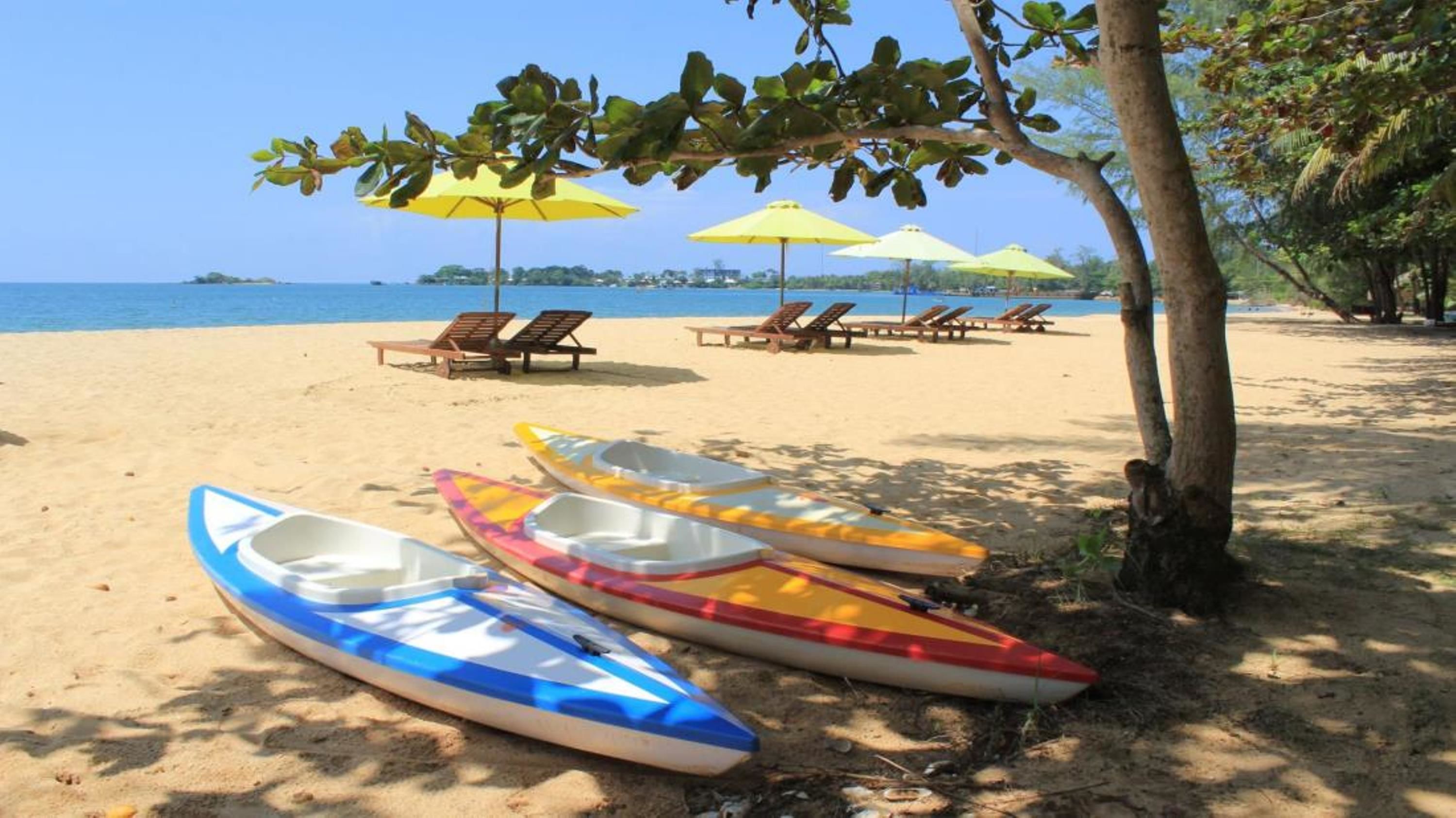 Una playa con varias kayaks y sillones de playa bajo sombrillas amarillas.