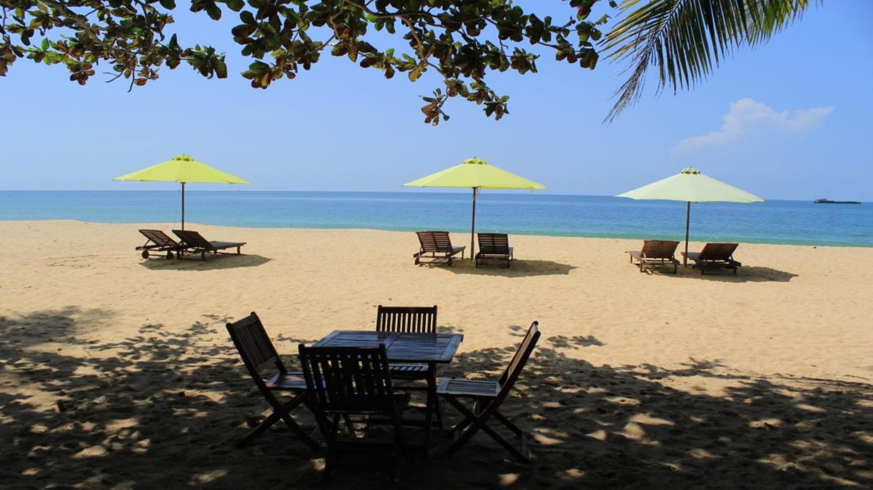 A beach with three umbrellas and lounge chairs, a table with chairs, and a view of the ocean.