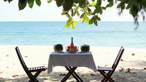 A beachside table with a white tablecloth, two chairs, and a bottle of water. - Vung Bau Resort (Phu Quoc)