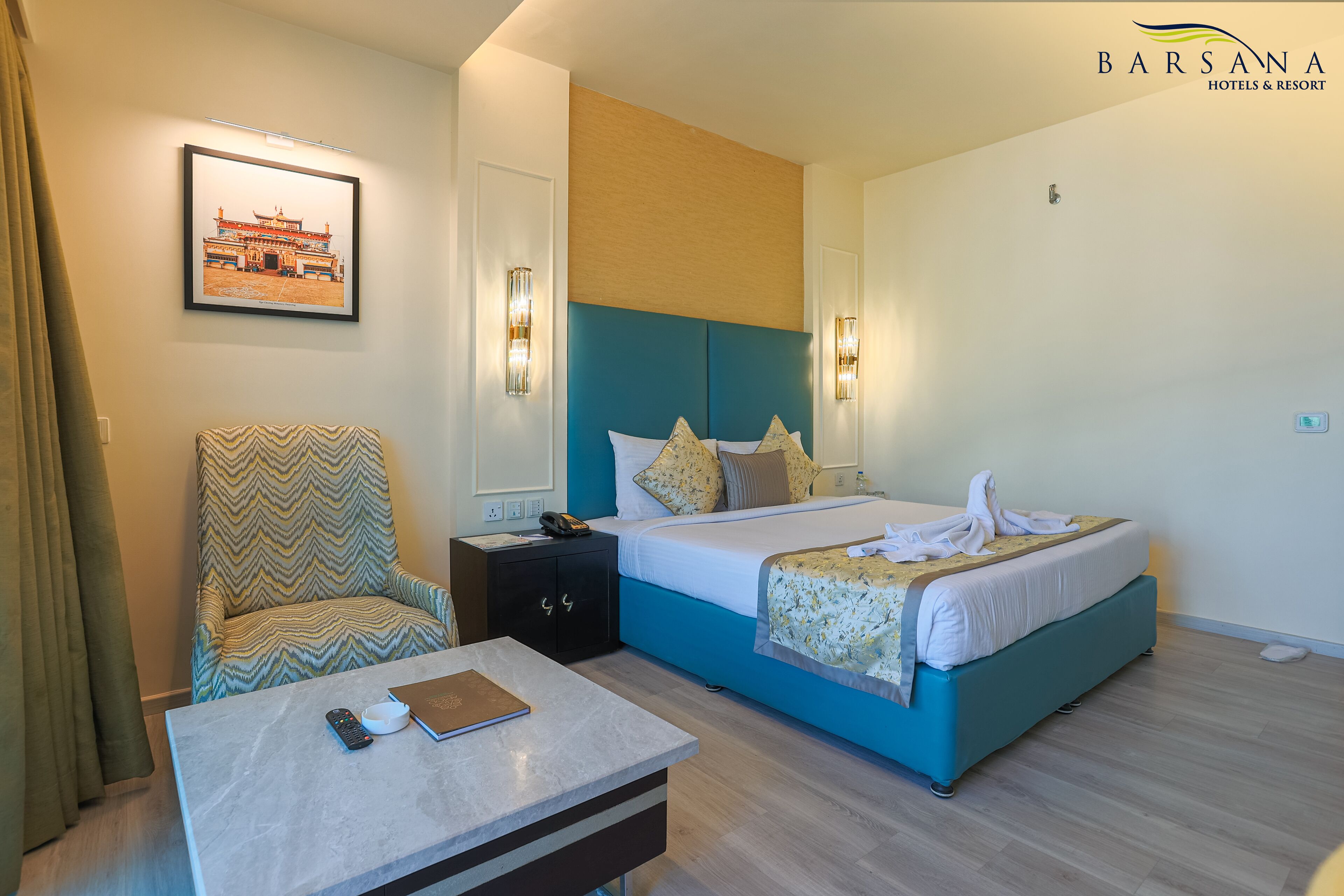 A hotel room with a bed, a chair, a bedside table, and a wall-mounted picture.