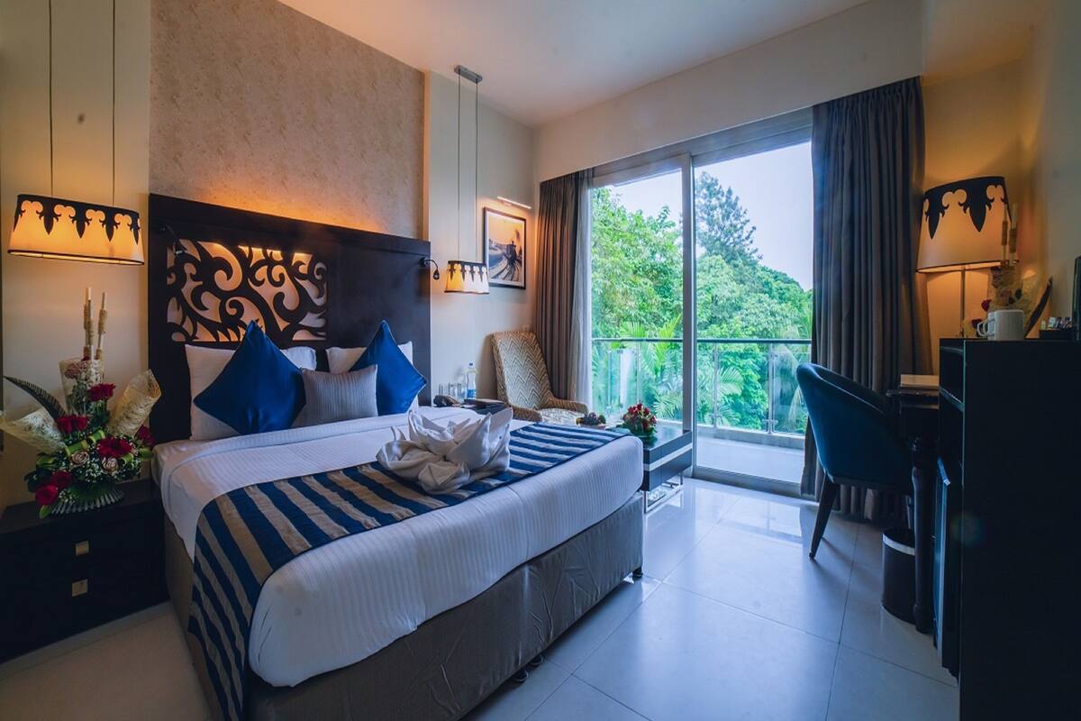 Une chambre d’hôtel avec un grand lit, un bureau, une chaise et un balcon donnant sur un paysage verdoyant.