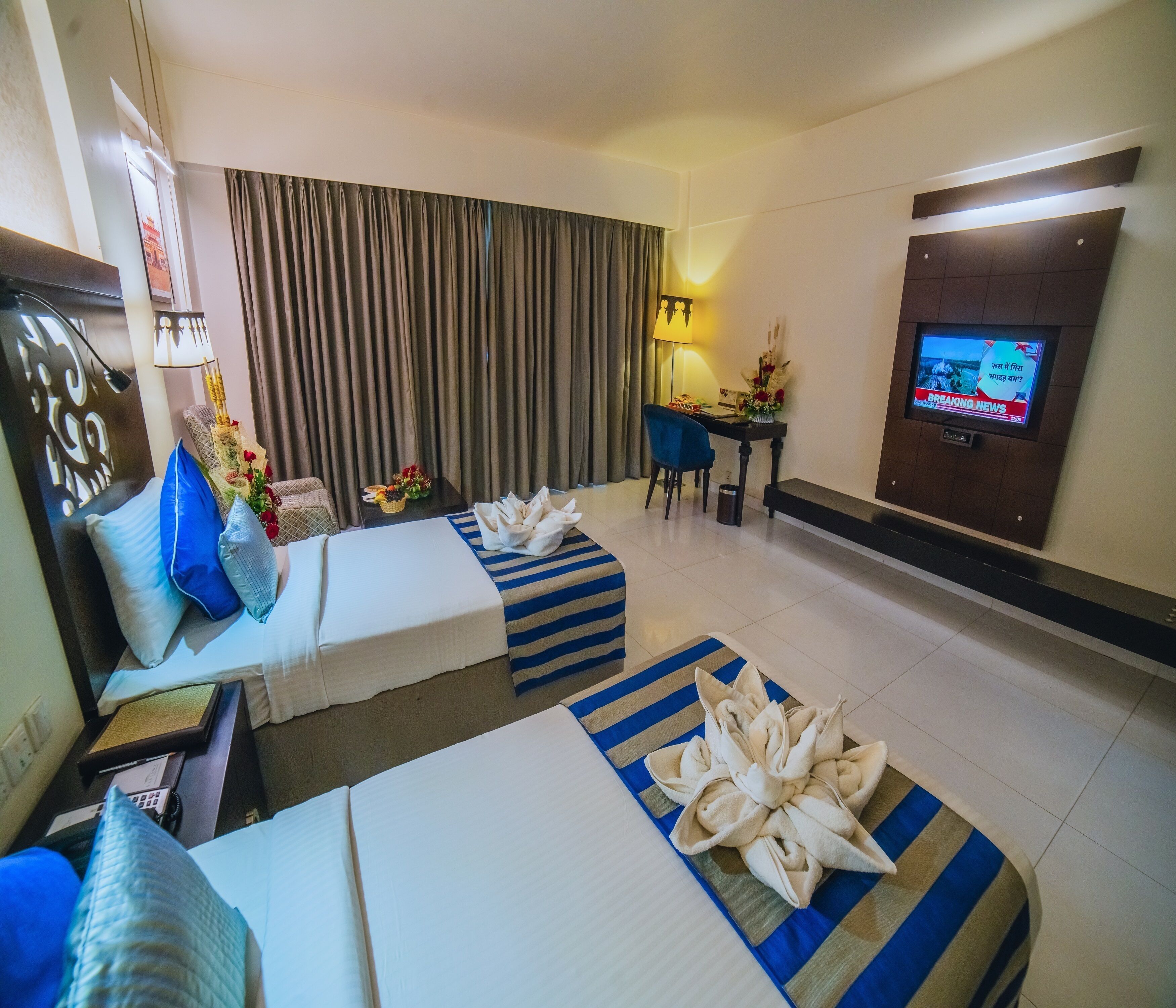 Una habitación de hotel con dos camas, televisión, escritorio con lámpara y cortina.