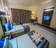 Una habitación de hotel con dos camas, televisión, escritorio con lámpara y cortina.