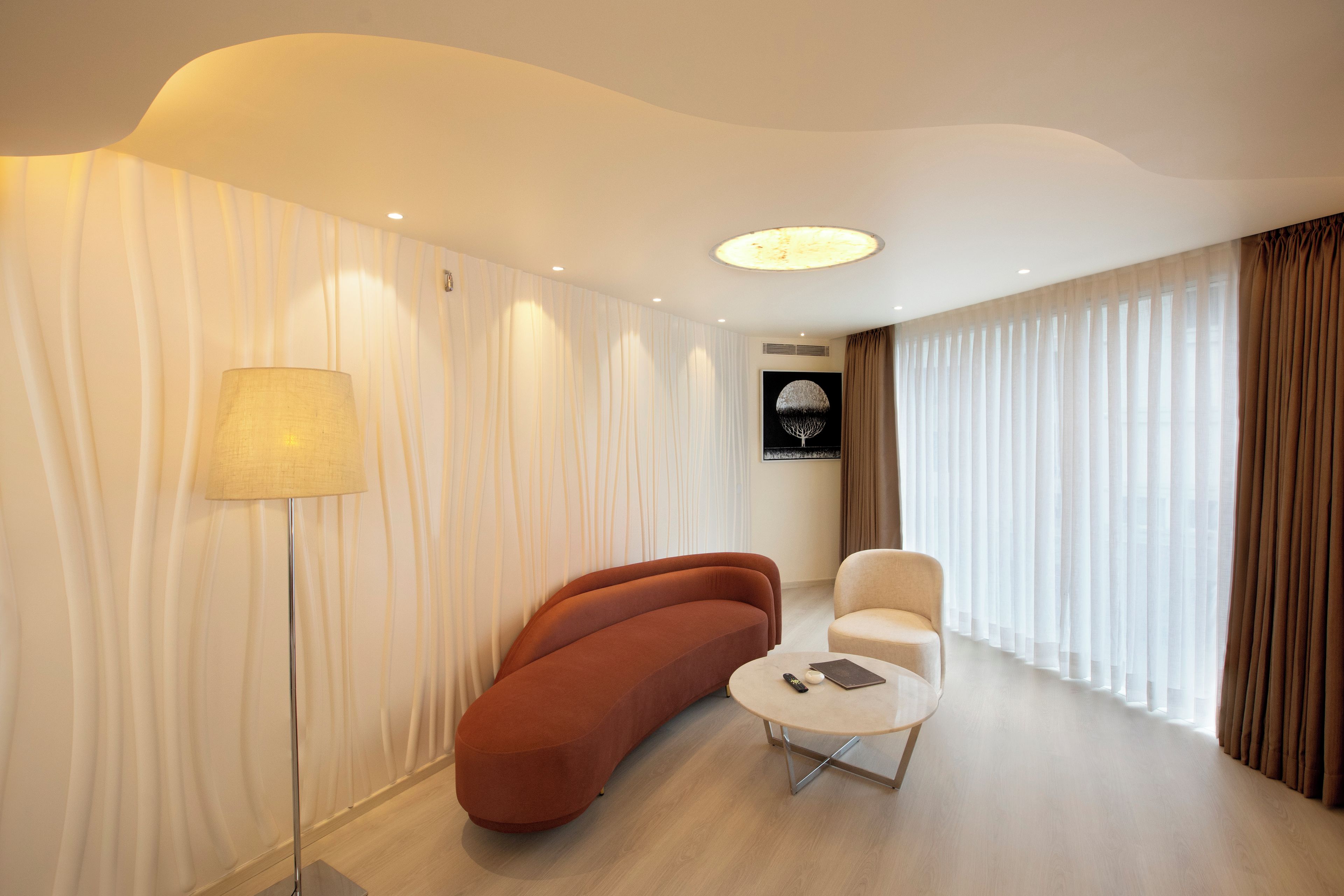 Une chambre d’hôtel moderne avec un canapé incurvé, une table ronde et un lampadaire.