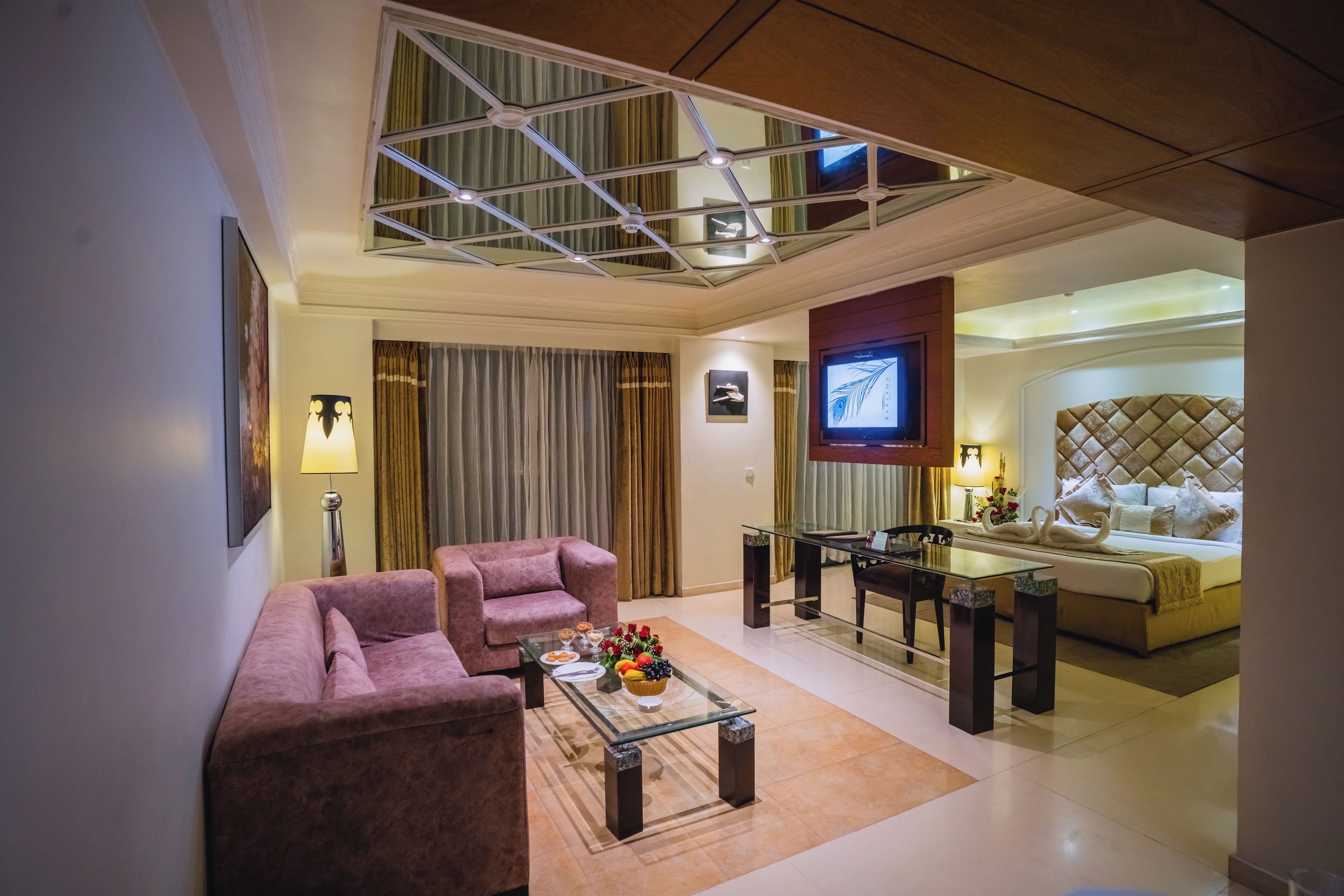 A modern living room with a glass coffee table, two armchairs, a television, and a dining area with a glass table and chairs.
