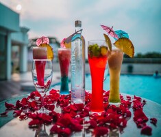 Un tavolo con diversi drink, alcuni decorati con ombrellini e guarnizioni, circondato da petali di rosa.