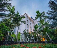 Un hotel con un cartello ben visibile con su scritto "BARSOLA", immerso in una vegetazione rigogliosa e palme.