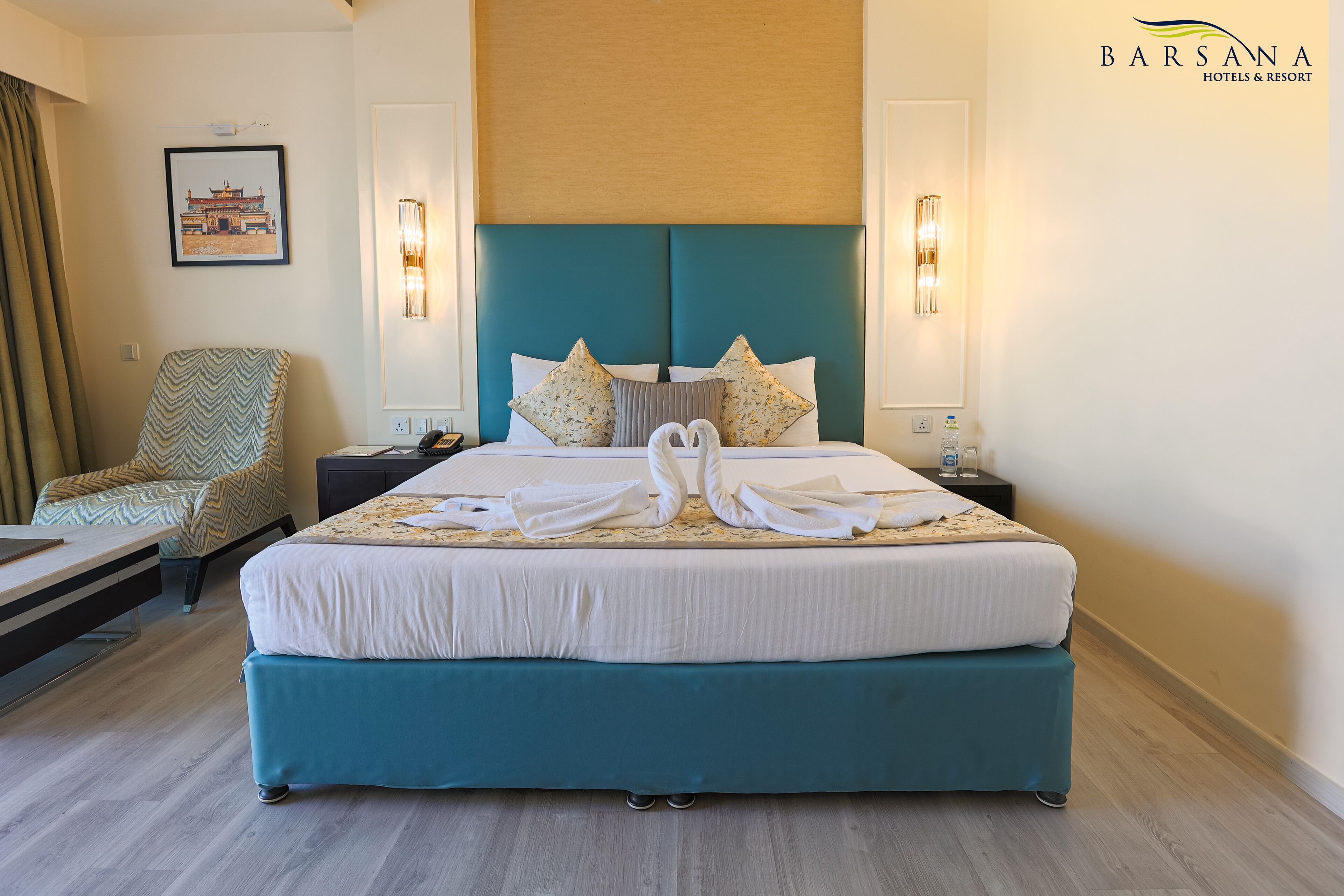 A hotel room with a large bed, a chair, a nightstand, and a wall-mounted light fixture.