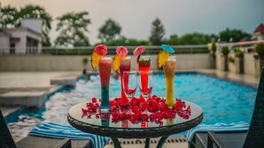 Une table placée au bord de la piscine, avec des boissons et des pétales de rose, entourée de chaises longues et d’une piscine.