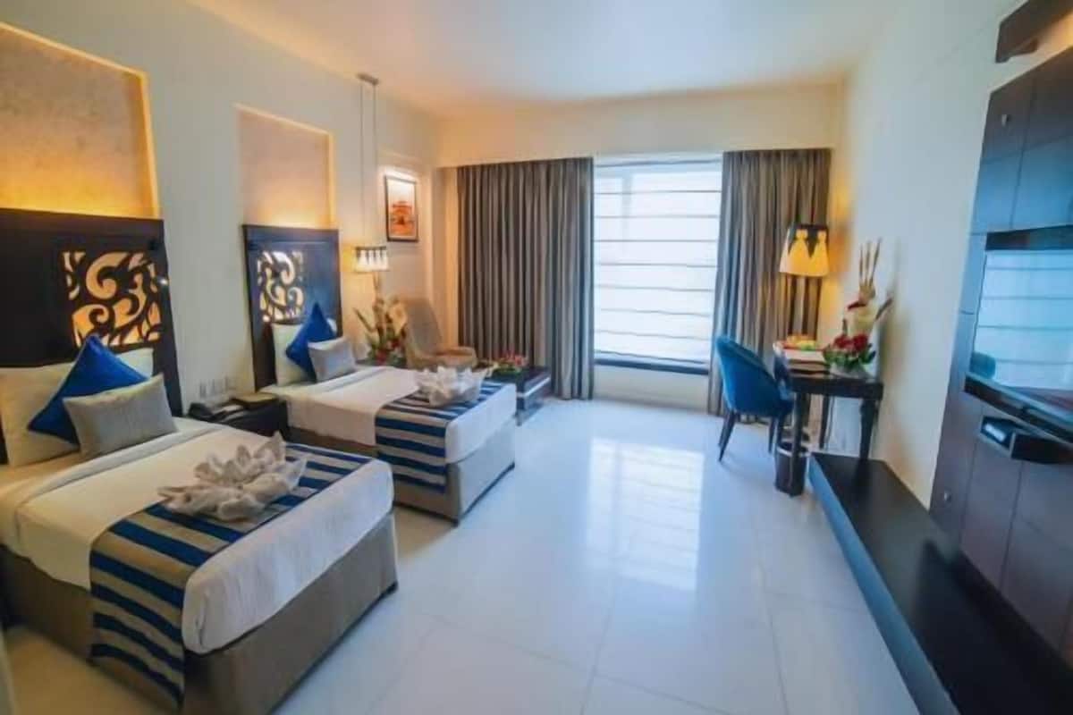 Une chambre d’hôtel avec deux lits, un bureau, une chaise et une télévision.