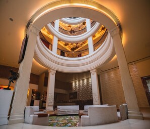 A grand, multi-level atrium with a central staircase, elegant columns, and a chandelier.