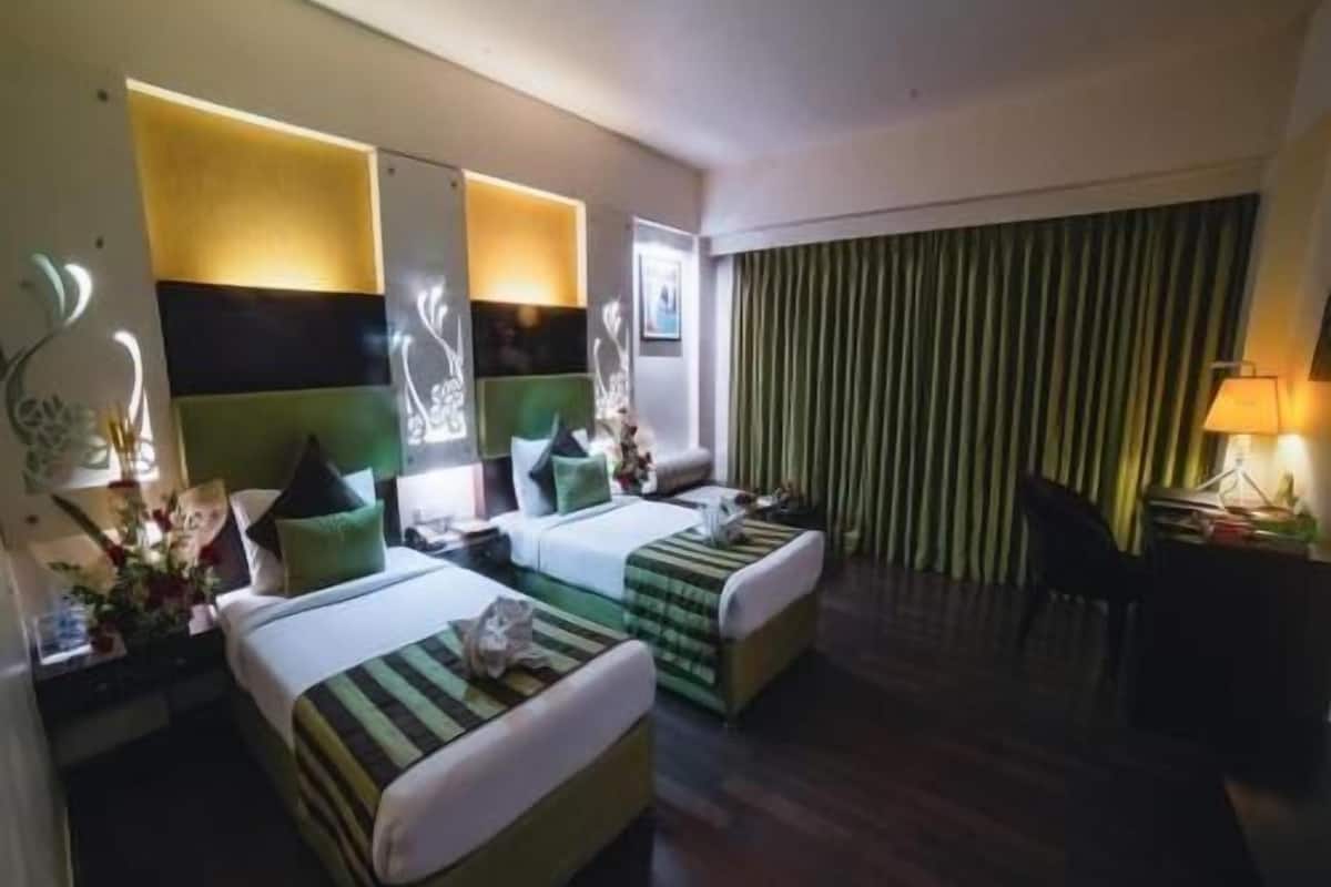 Une chambre d’hôtel avec deux lits, un bureau, une chaise et une grande fenêtre avec des rideaux.