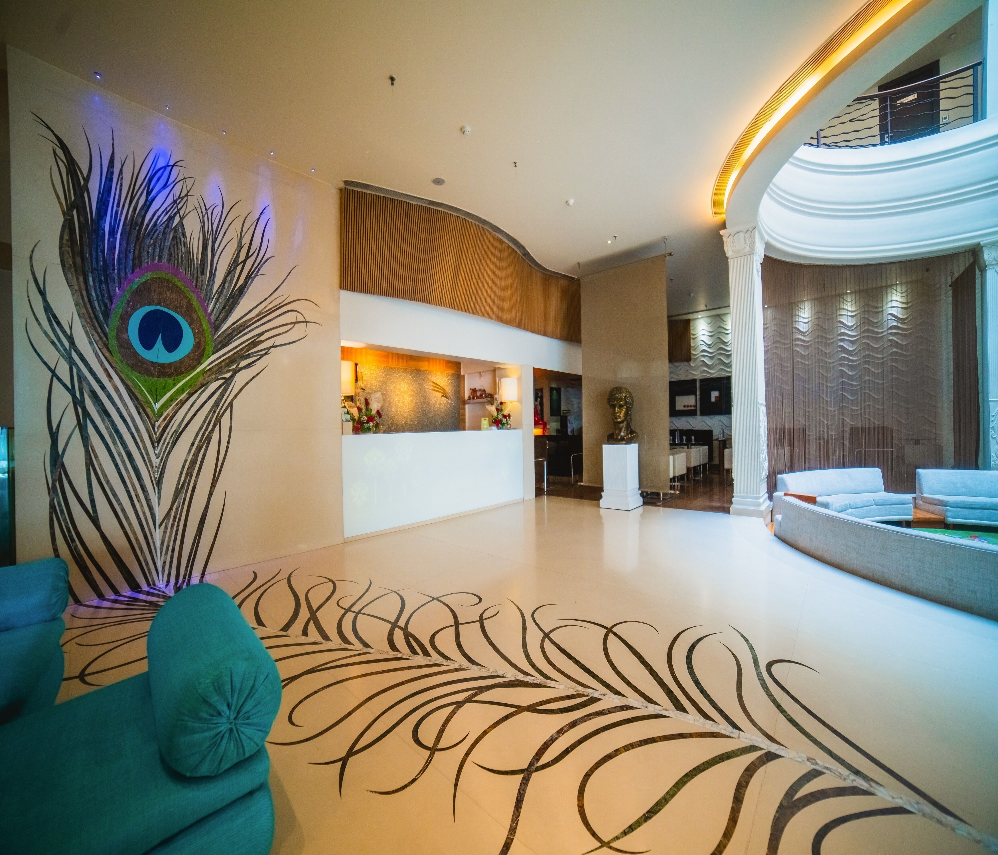 Een moderne hotellobby met een muurschildering van een pauwenveer, een receptiebalie en een zithoek met een bank en fauteuils.