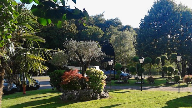 Un parc bien entretenu, avec des pelouses impeccables, différentes espèces d’arbres et quelques voitures garées.