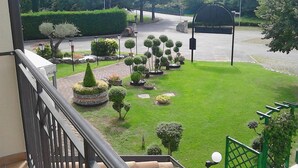 Un jardin bien entretenu, avec des haies taillées avec soin et des arbres taillés en forme de boule, un chemin pavé et une clôture verte.