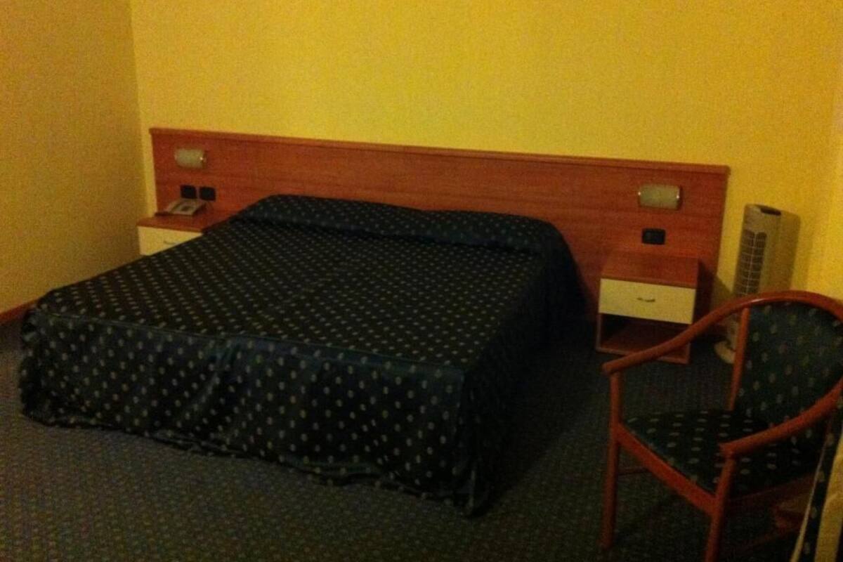 A hotel room with a bed, a wooden headboard, a bedside table with a phone, and a chair.
