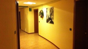 Un couloir d’hôtel avec un sol carrelé, un panneau de signalisation de sortie vert, une porte et un tableau accroché au mur.