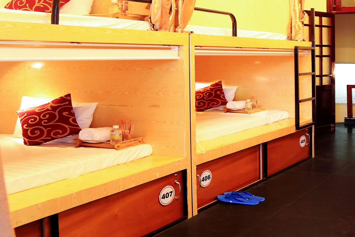 Ein Schlafsaalzimmer mit Stockbetten, Holz-Kopfteilen und einem kleinen Tisch mit einer Flasche und Gläsern.