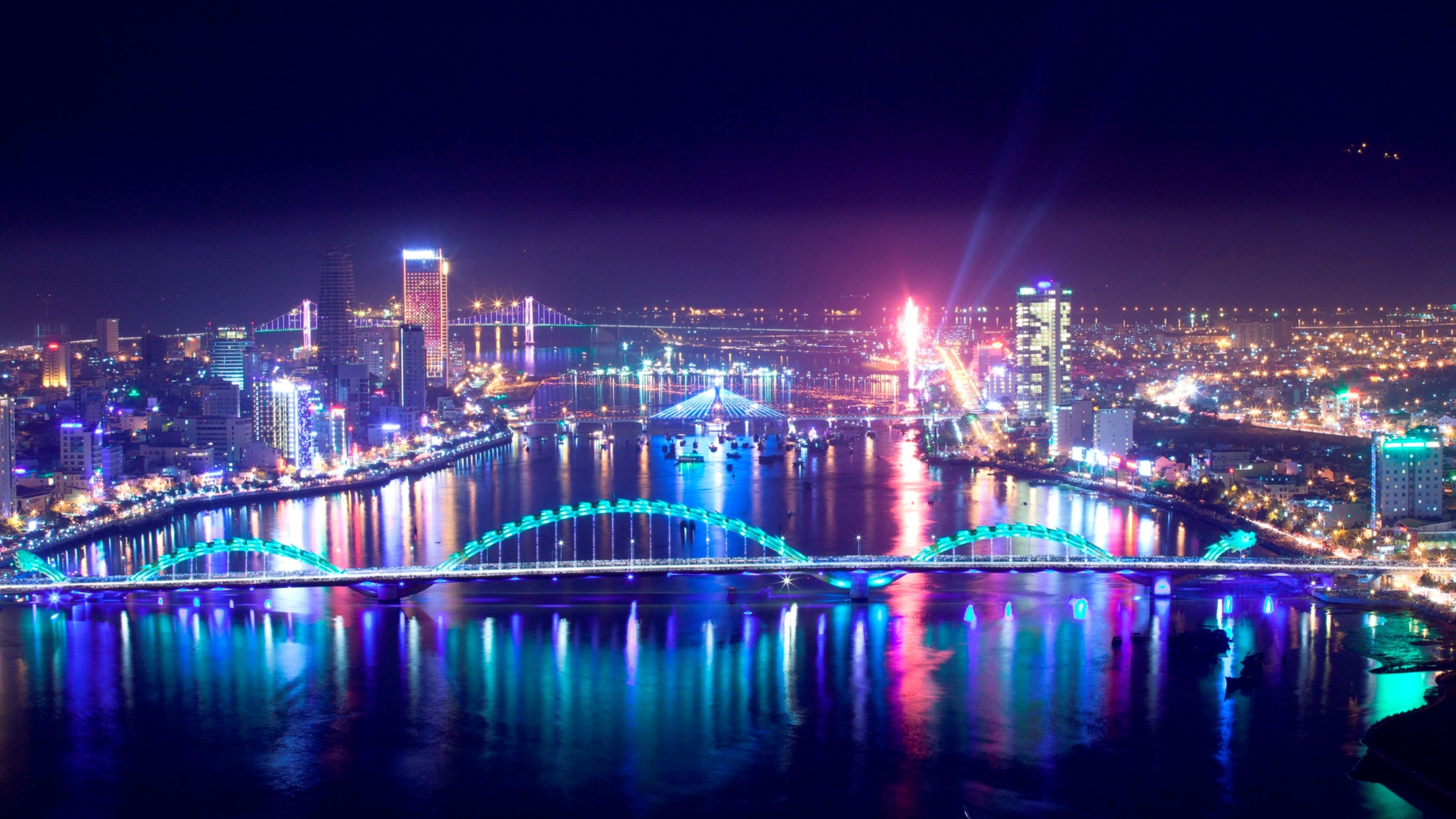 A nighttime cityscape with illuminated bridges and buildings reflecting on the water.