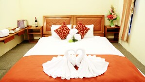 A hotel room with a neatly made bed, a wooden headboard, a bedside table with a wine bottle, and a nightstand with a vase of flowers. - Like Backpacker Hostel (Da Nang)