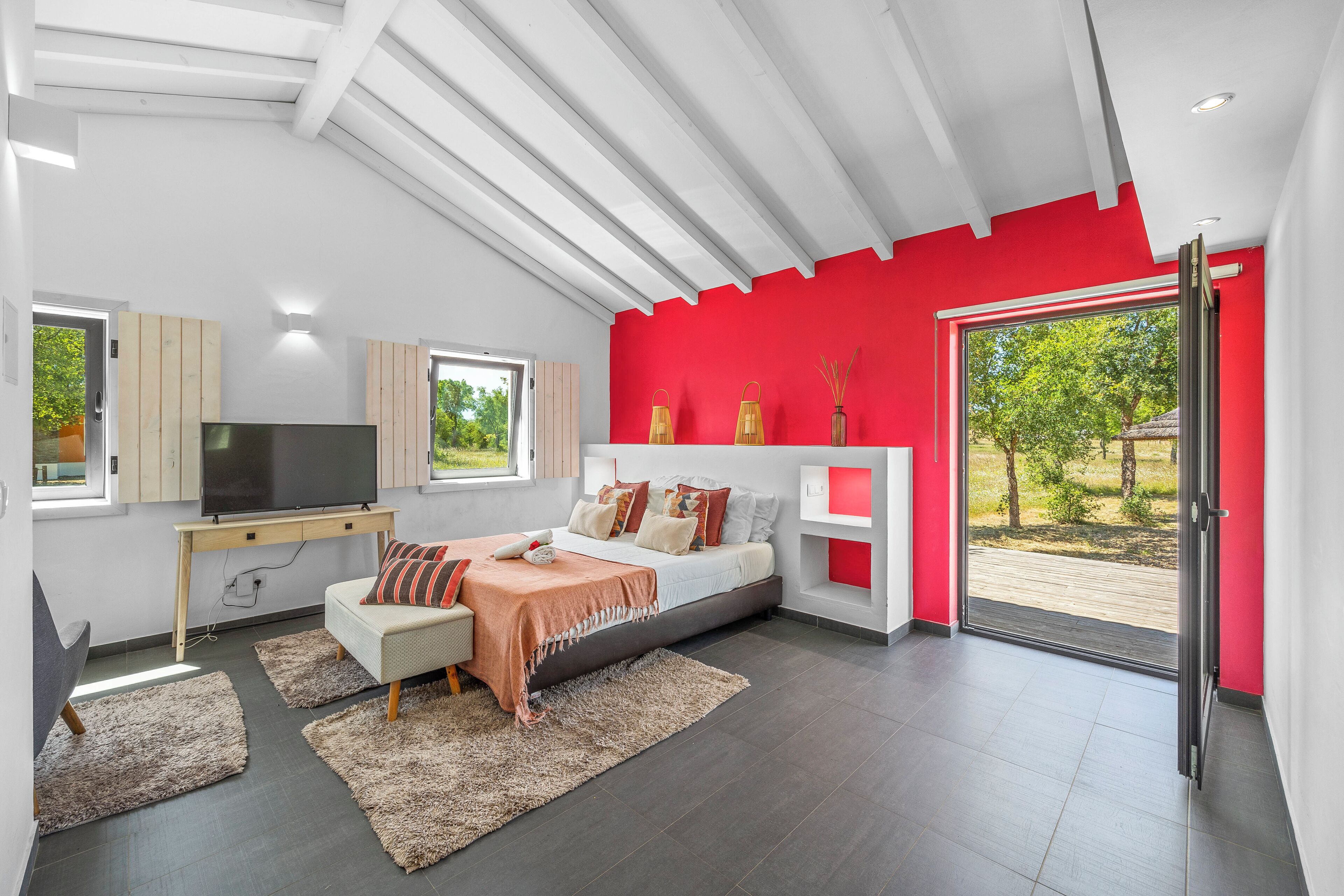 Un dormitorio moderno con cama, televisor y un ventanal grande.