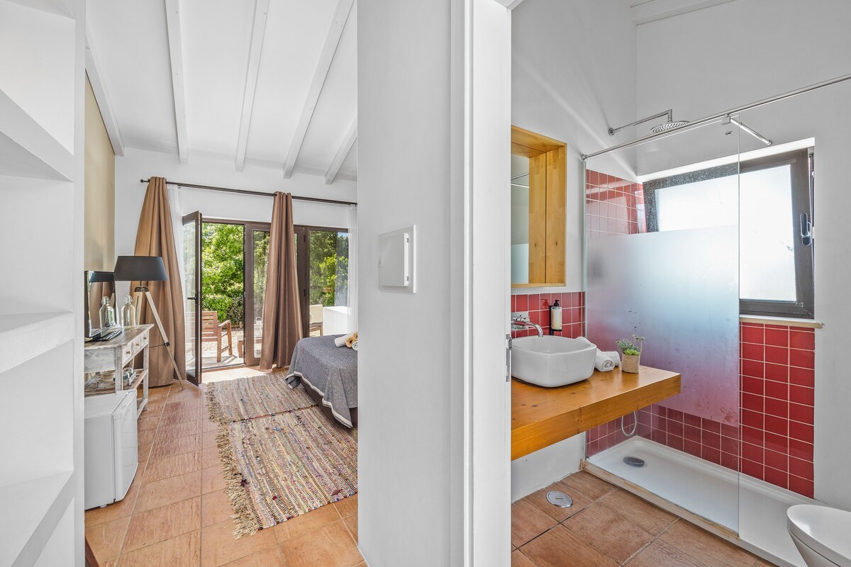 A bedroom with a bed, a desk, and a window. The bathroom has a shower, a sink, and a toilet.
