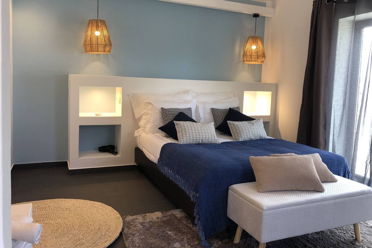 A modern bedroom with a large bed, two bedside tables, a small sofa, and two hanging lamps.
