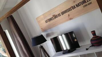 Una habitación con pared blanca, un letrero de madera con texto, una lámpara negra, un objeto metálico y un florero estampado.