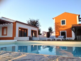 Una piscina con agua cristalina que refleja los edificios. Hay sillas de descanso y una mesa cerca de la piscina.