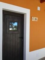 A dark wooden door with a small window, a white wall with an orange lower half, and a sign reading "POEJOS" on the wall.