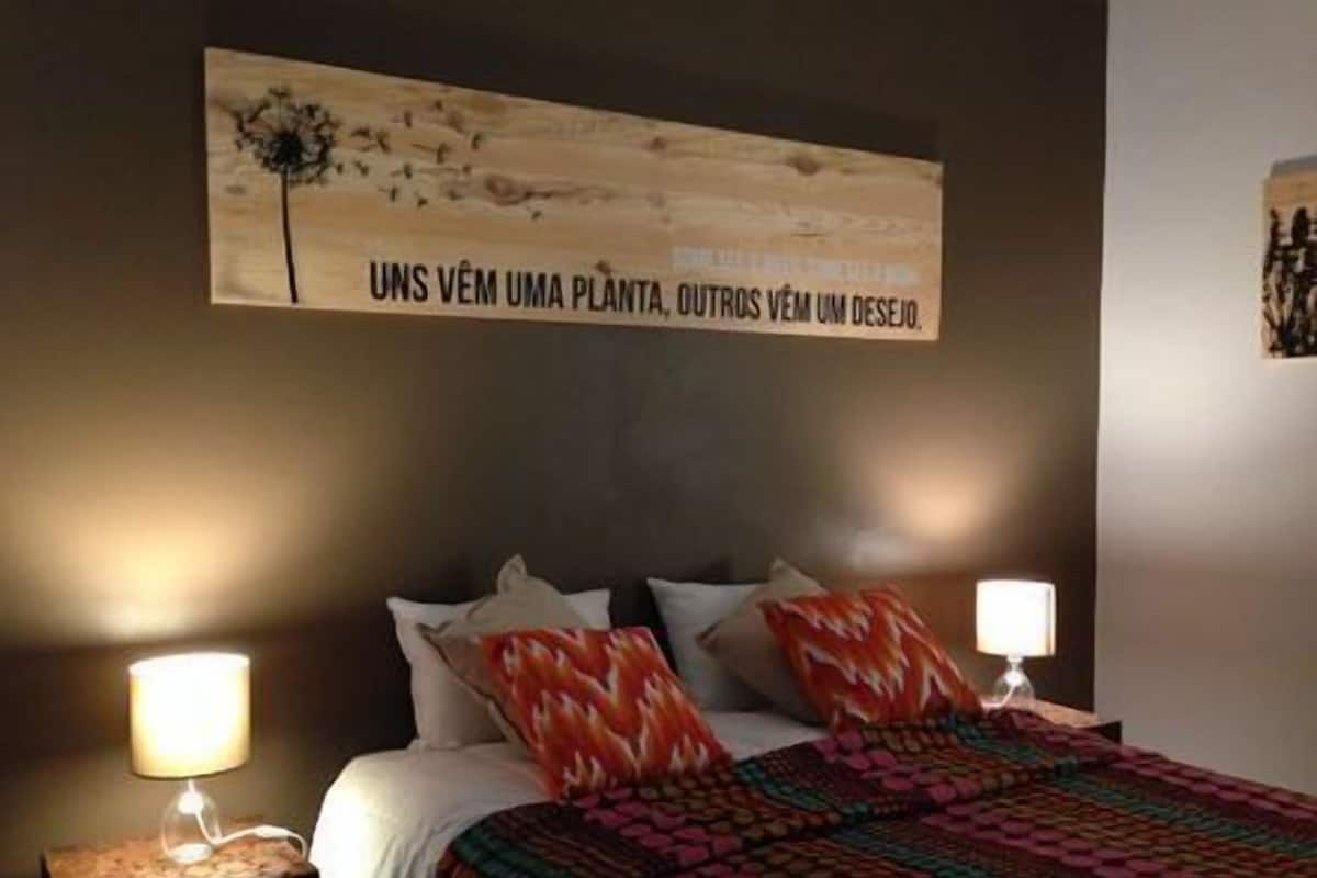 A bedroom with a bed, two bedside lamps, a colorful blanket, and a wall with a painting.
