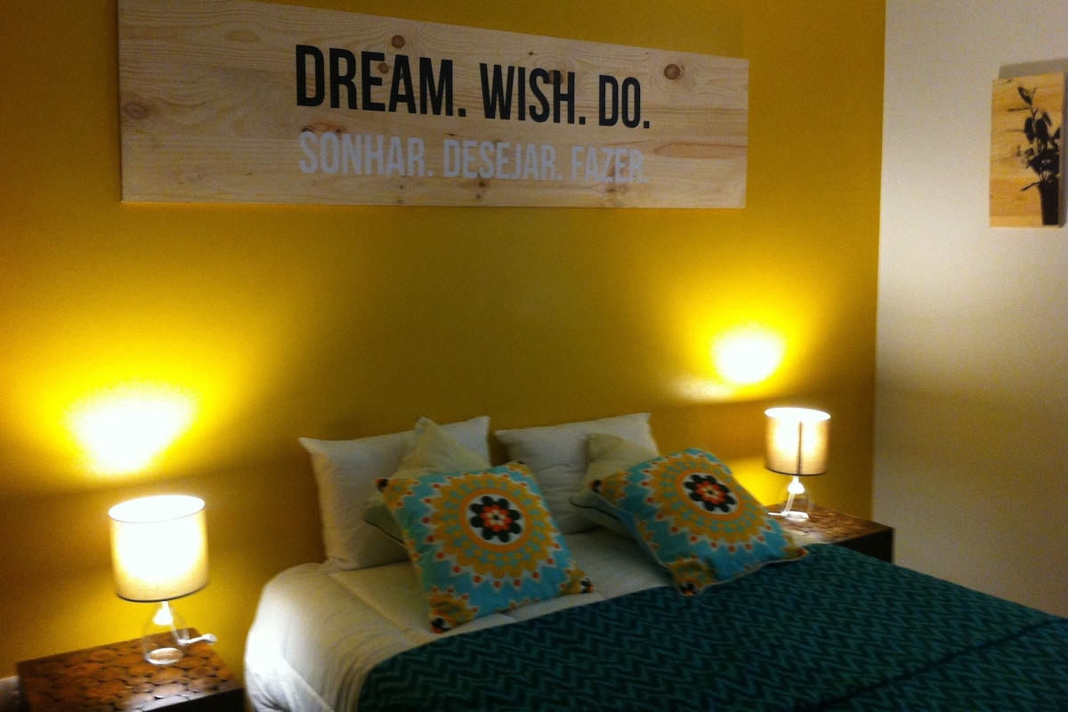 A hotel room with a bed, two bedside lamps, and a sign on the wall.