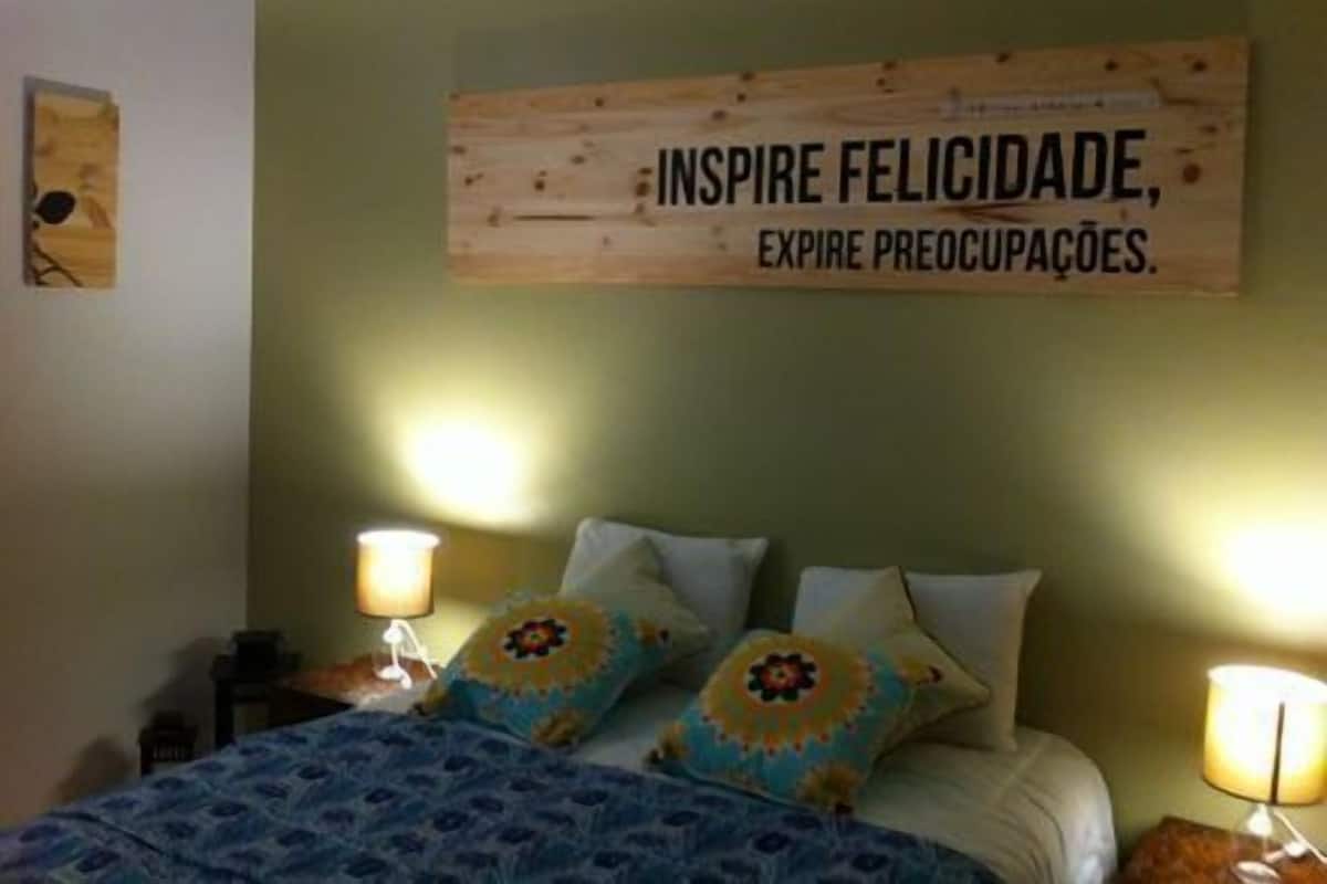 A bedroom with a bed, two bedside lamps, and a wall-mounted sign with a motivational quote.