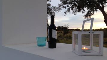 Eine Weinflasche, ein Glas und ein Laternenlicht auf einem Vorsprung mit Blick auf Bäume und einen Sonnenuntergang.