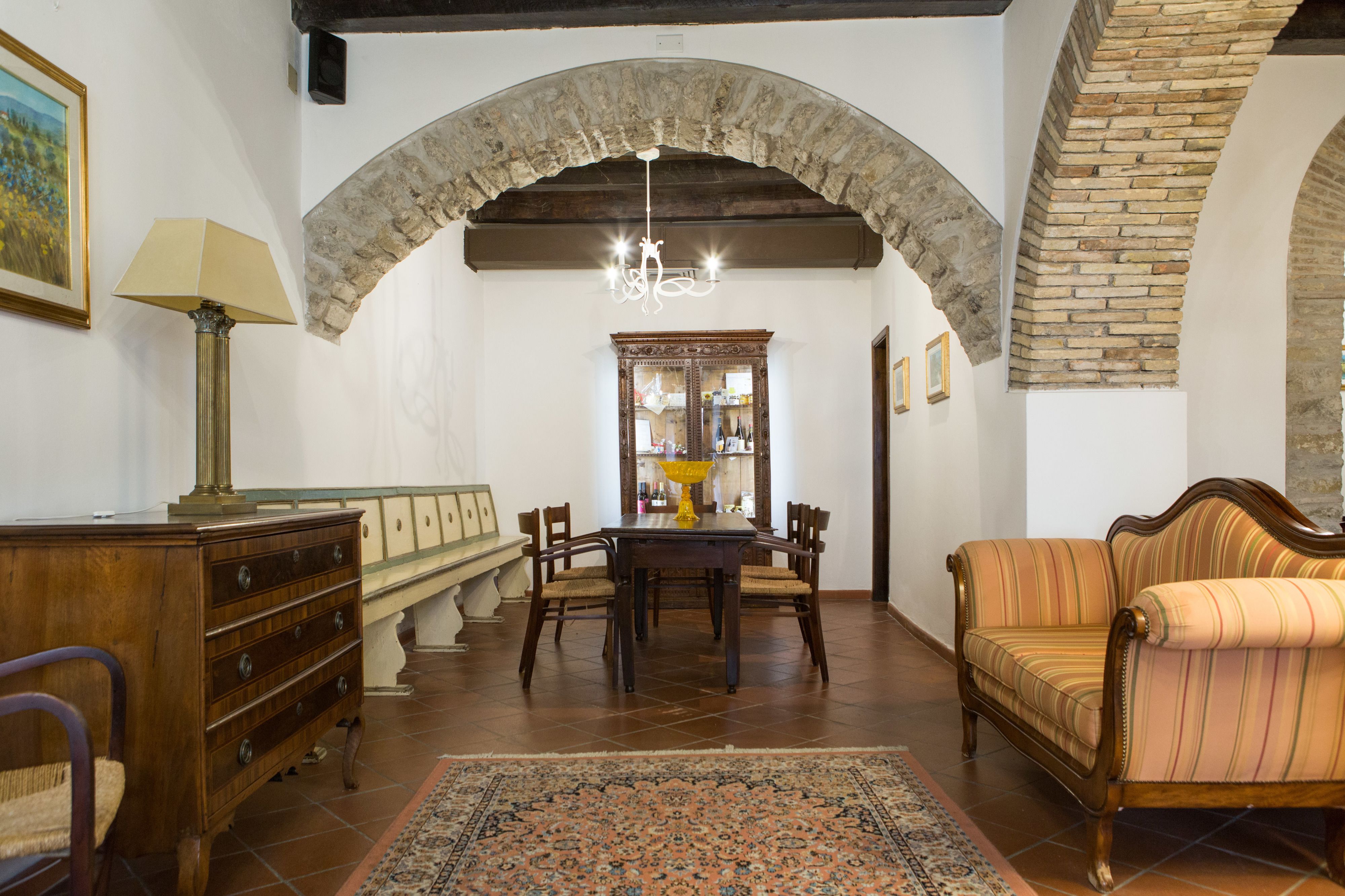 A room with a stone archway, a chandelier, a wooden table with chairs, a sofa, and a patterned rug.