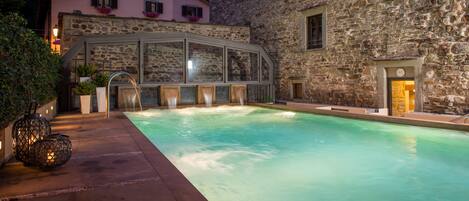 Relax by the serene pool surrounded by rustic stone buildings and a well-maintained patio.