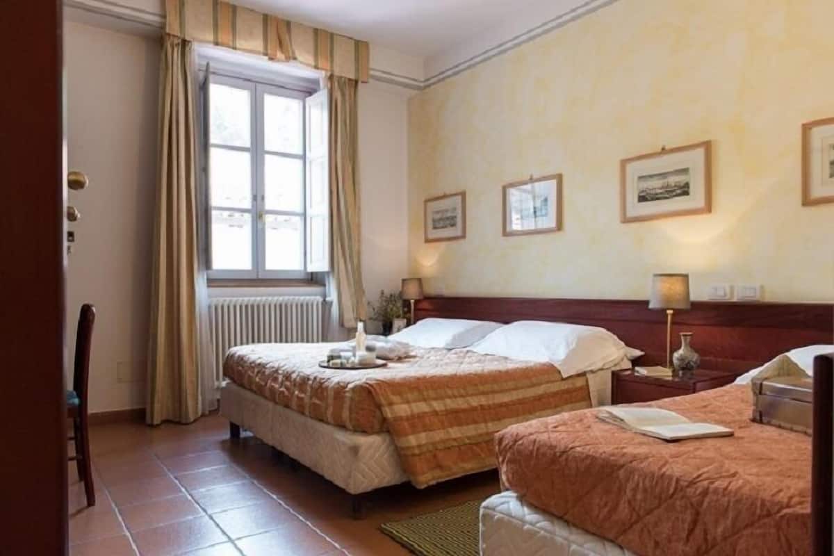 Habitación de hotel con dos camas, una ventana con cortinas, cuadros en la pared y un radiador.