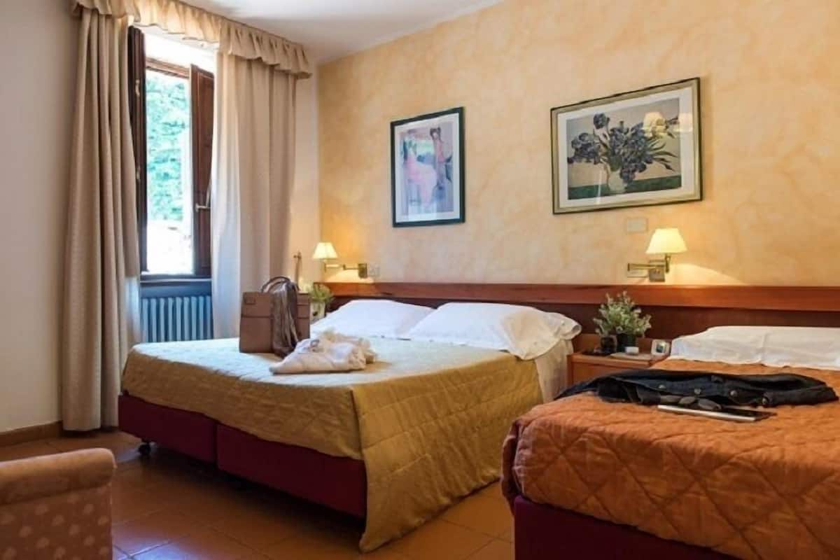 Habitación de hotel con cama, una silla, una mesita de noche y dos cuadros en la pared.