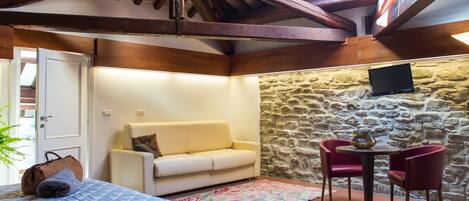 Una habitación acogedora con cama, sofá, pared de piedra y una pequeña mesa con sillas.