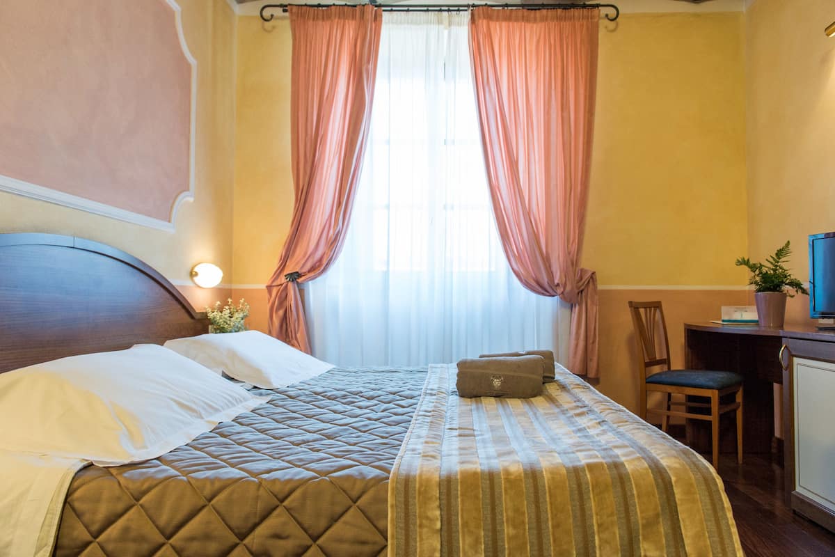 Habitación de hotel con cama, cortinas, escritorio con computadora y una silla.